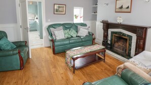 A spacious living room with a green leather sofa, a wooden coffee table, and a fireplace. - Tí Coilín Mhac (Maumeen)
