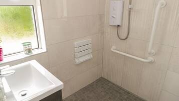 A bathroom with a white sink, a window, a towel rack, a shower with a grab bar, and a toilet.