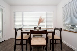 A dining area with a table and four chairs, a vase with dried flowers, and large windows with blinds. - Harbor House A, overlooking Santa Cruz Harbor (Santa Cruz)