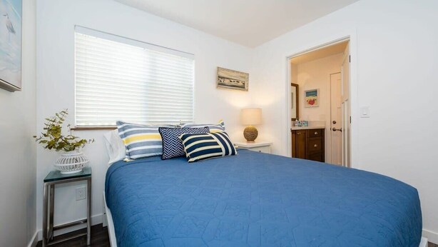 A bedroom with a large bed, a window with blinds, a bedside table with a lamp, and a door leading to another room. - Harbor House A, overlooking Santa Cruz Harbor (Santa Cruz)