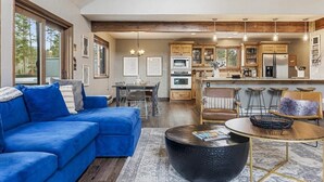 Een moderne woonkamer met een blauwe modulaire bank, een ronde salontafel en een eethoek met een houten tafel en stoelen.