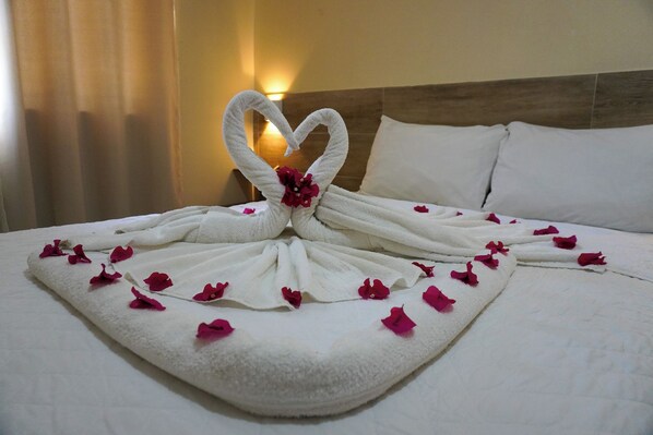A bed with a towel arranged in a heart shape, decorated with rose petals and a flower. - Pousada Donna Maraka (Ipojuca)
