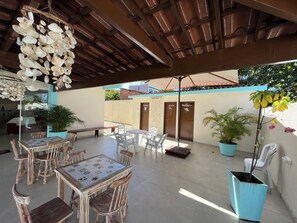 An outdoor patio area with wooden tables and chairs, a hanging shell decoration, and potted plants. - Pousada Donna Maraka (Ipojuca)