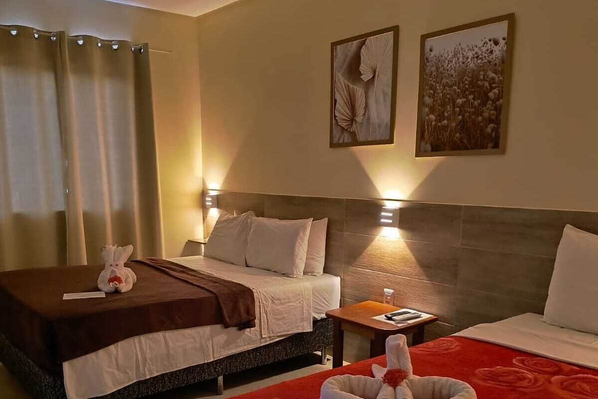 A hotel room with two beds, a red carpet, a small table, and two wall-mounted lamps.
