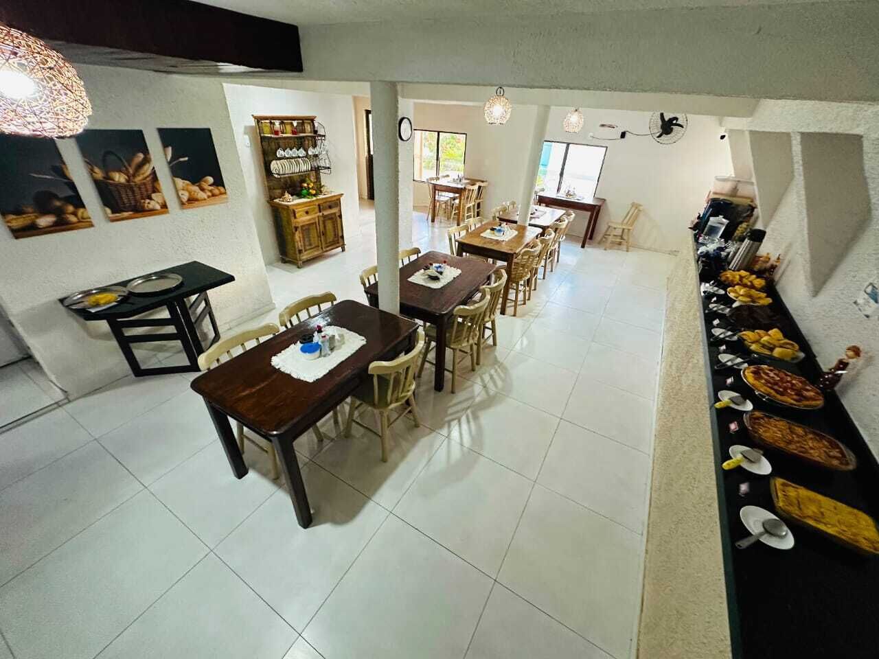 A spacious dining area with multiple tables and chairs, a buffet line with various dishes, and a kitchen area in the background.