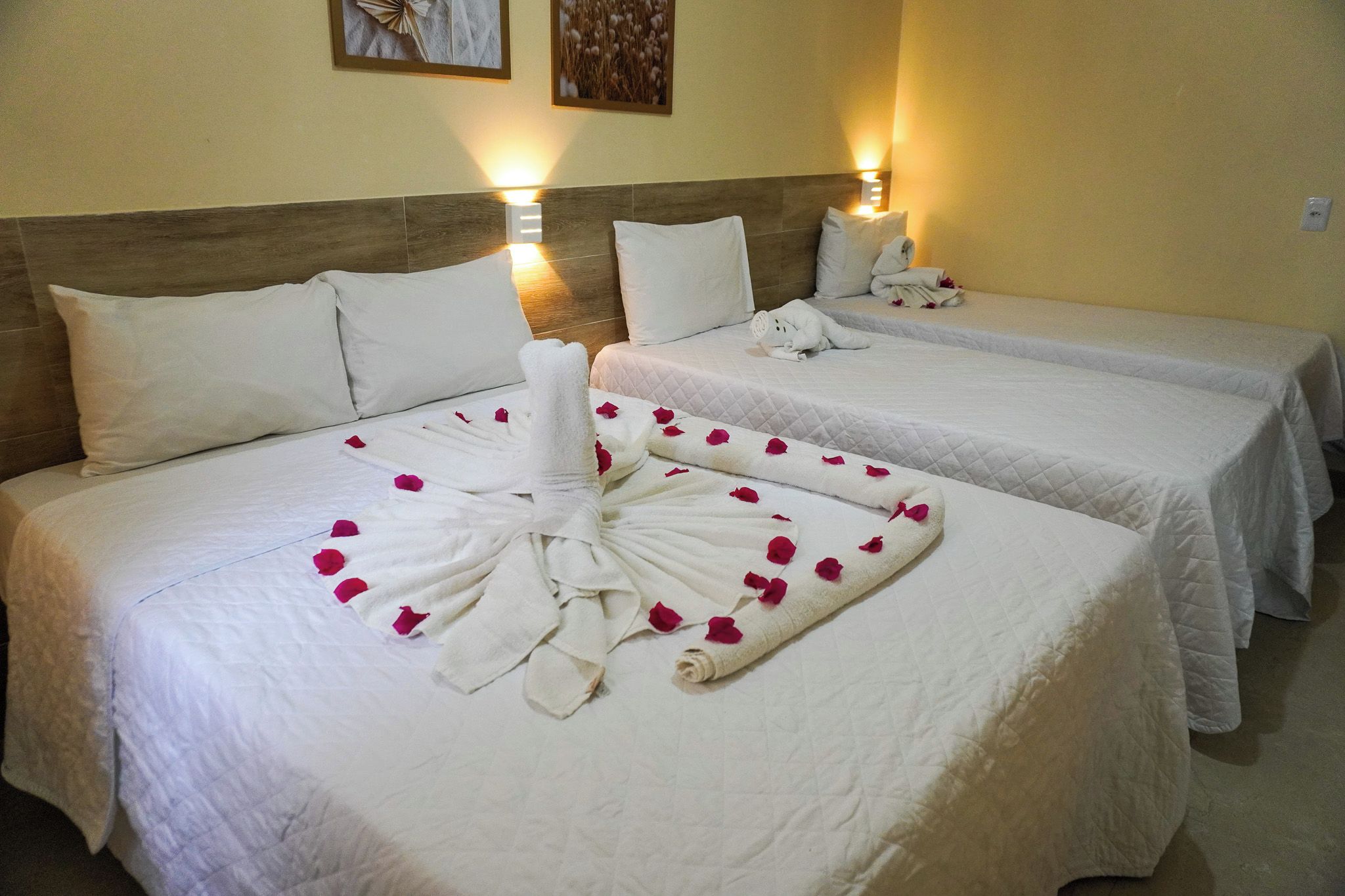 A hotel room with two beds, each with white linens and pillows, and a decorative towel arrangement with rose petals.