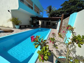 A swimming pool with a tiled deck, surrounded by potted plants and a building with a balcony. - Pousada Donna Maraka (Ipojuca)