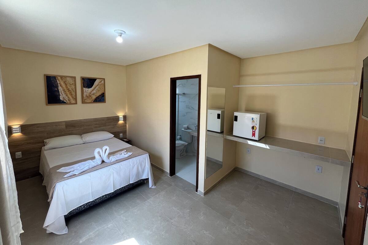A hotel room with a bed, a nightstand, a mirror, a shelf, and a door.