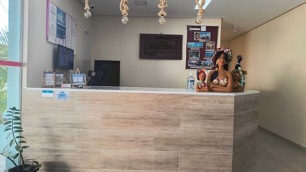 A reception desk with a light wood finish, a computer monitor, and a telephone. There are informational posters on the wall and a potted plant to the left.