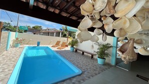 Ein Poolbereich mit blauem Pool, Liegestühlen und hängenden Muscheln.