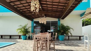 An outdoor patio area with a wooden table and chairs, potted plants, and a pool. - Pousada Donna Maraka (Ipojuca)