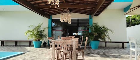 Un patio al aire libre con mesa y sillas de madera, plantas en macetas y una piscina.