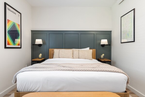 Un dormitorio ordenado con una cama grande, dos mesitas de noche con lámparas y cuadros en las paredes.