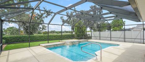 A covered swimming pool with a metal roof structure, surrounded by a fence and a well-maintained lawn.