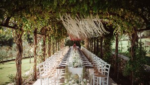 An outdoor wedding setup with a long table, white chairs, and floral decorations. - Agriturismo Vecchia Quercia (Poppi)