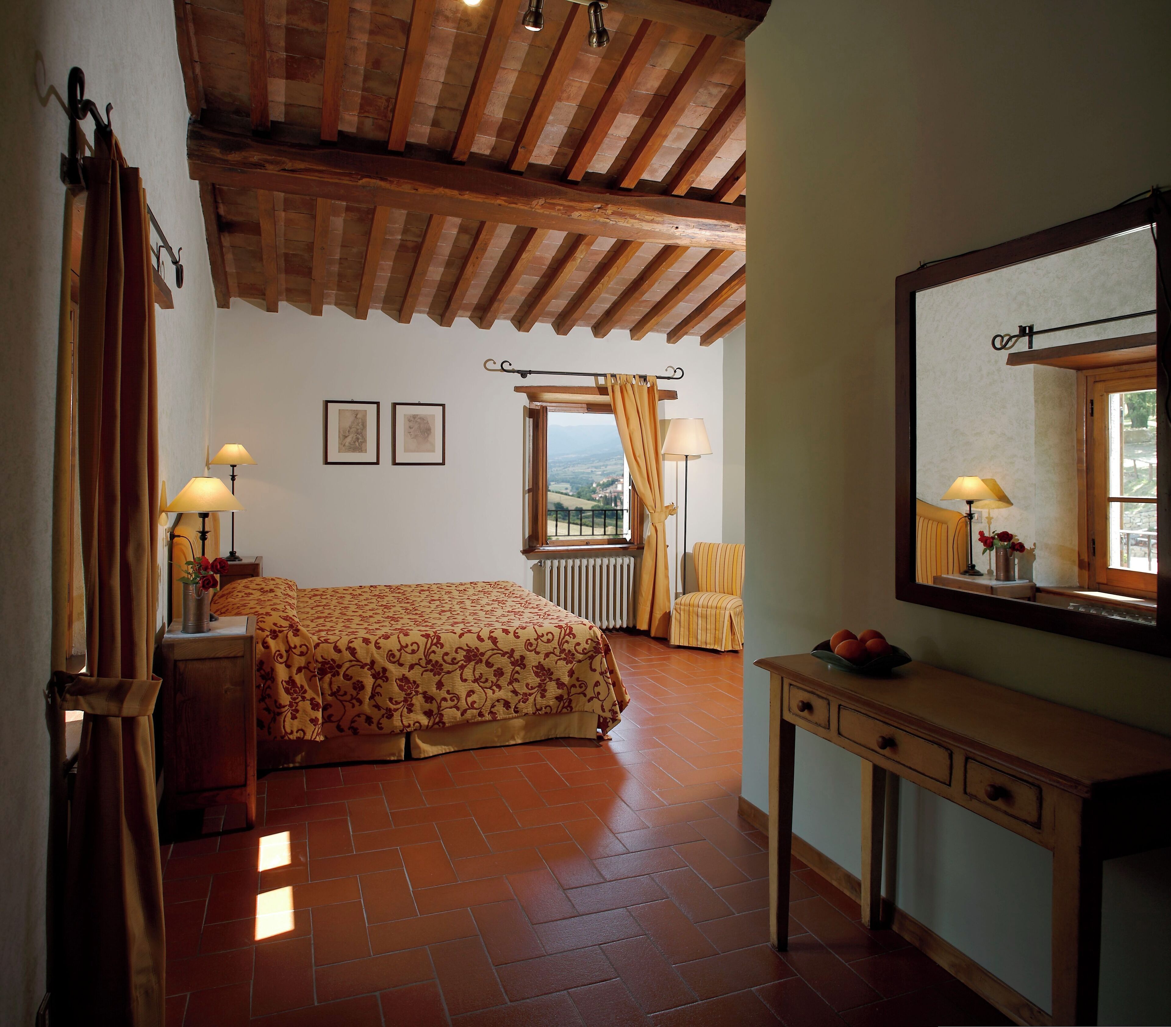 A bedroom with a bed, a wooden desk, a chair, a window with curtains, and a view of the outdoors.