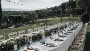 A long table set for a formal outdoor event with a view of a vineyard and hills in the background. - Agriturismo Vecchia Quercia (Poppi)