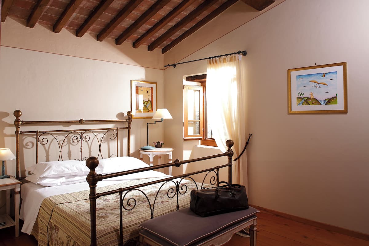 Quarto com estrutura de cama de madeira, mesa de cabeceira, abajur e um quadro na parede.