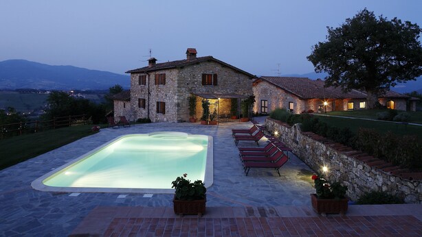 A stone house with a swimming pool, outdoor seating, and a view of the mountains. - Agriturismo Vecchia Quercia (Poppi)