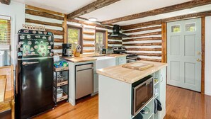 A compact kitchen with wooden beams, a refrigerator, a stove, and a microwave. - Modernized Log Cabin w Hot Tub, Fire Pit & Views! (Berkeley Springs)