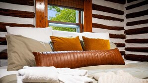 A log cabin-style bedroom with a bed, pillows, and a window. - Modernized Log Cabin w Hot Tub, Fire Pit & Views! (Berkeley Springs)