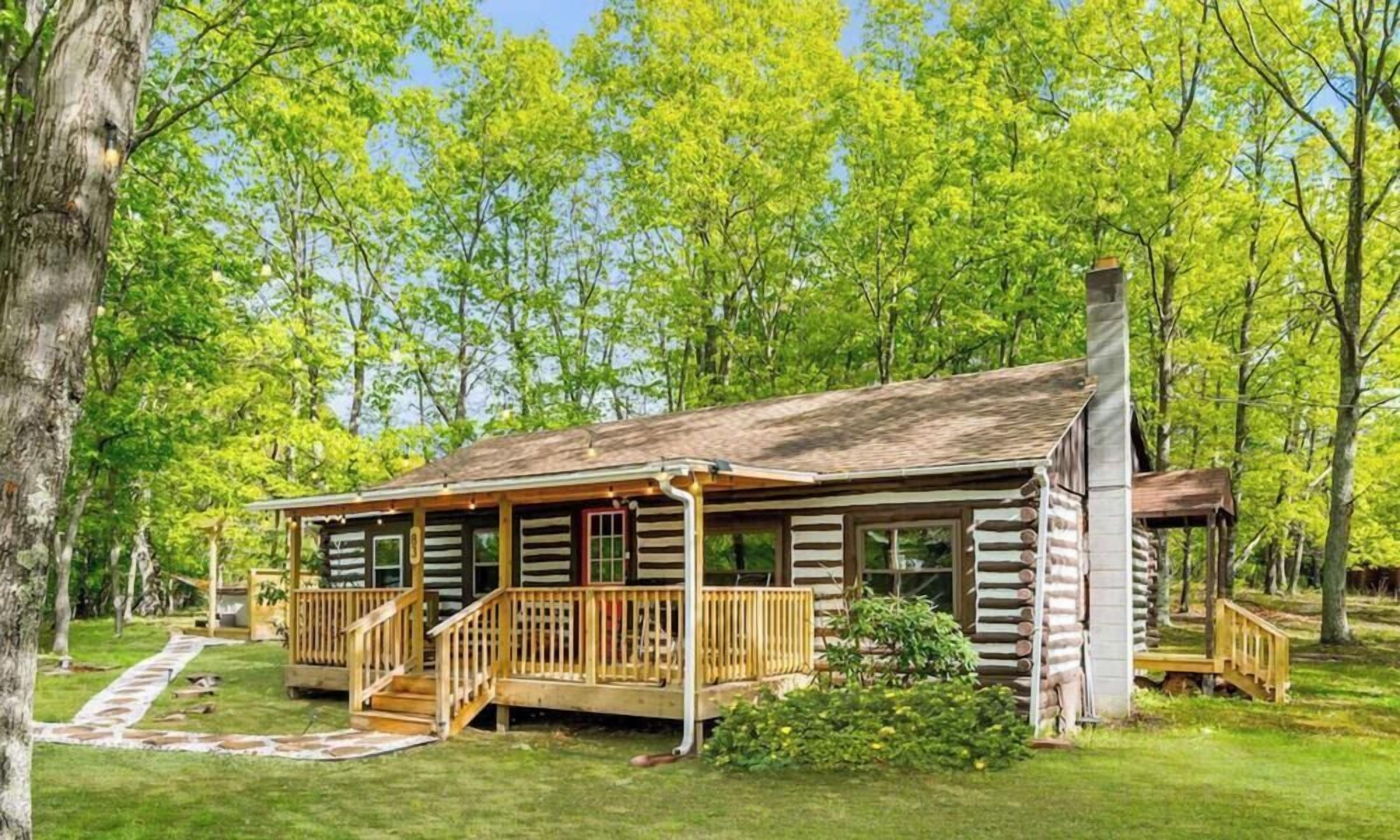 A log cabin with a porch, a chimney, and a small deck.