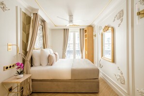 A bedroom with a bed, curtains, a bedside table with flowers, a ceiling fan, and a window with a view.