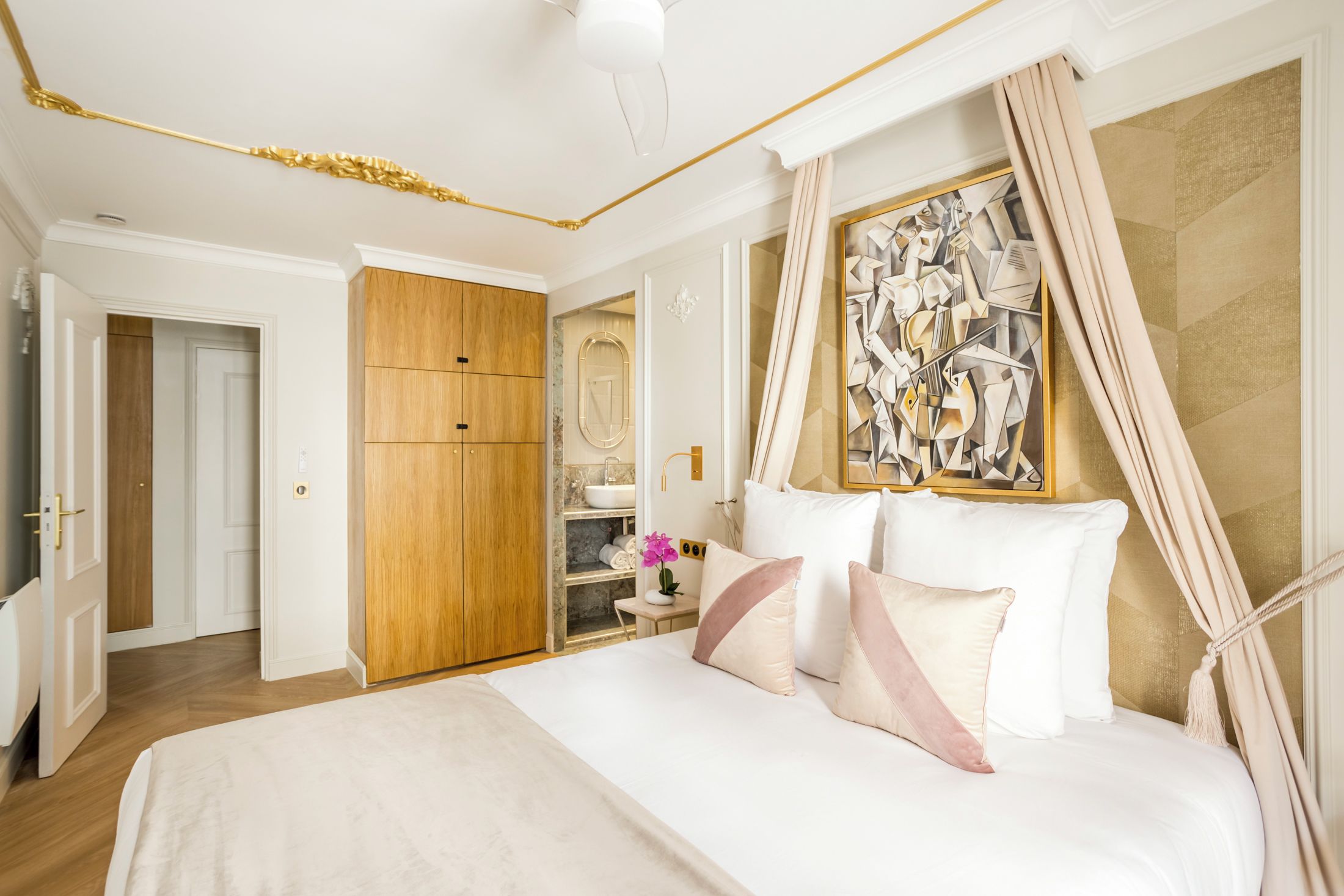 Une chambre à coucher avec un grand lit, une armoire en bois, une coiffeuse avec un miroir et un tableau accroché au mur.