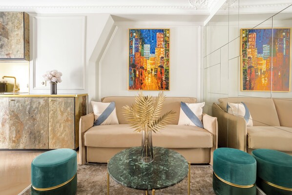 A modern living room with a beige sofa, teal ottomans, a glass coffee table, and two vibrant cityscape paintings on the walls.
