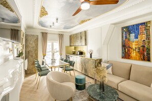 A modern living room with a sofa, a dining table with chairs, a kitchen area, and a ceiling fan.
