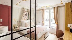 Une chambre d’hôtel avec un grand lit, un bureau, une chaise, une salle de bain avec baignoire et une fenêtre avec des rideaux.