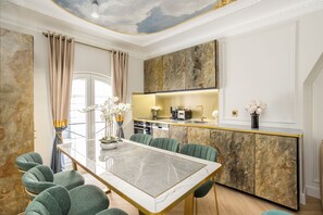 A modern dining area with a marble table, green upholstered chairs, and a kitchen with a marble backsplash.