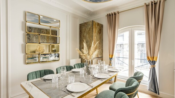 Une salle à manger avec une table en marbre, des chaises recouvertes d’un tissu vert et un élément décoratif mural.