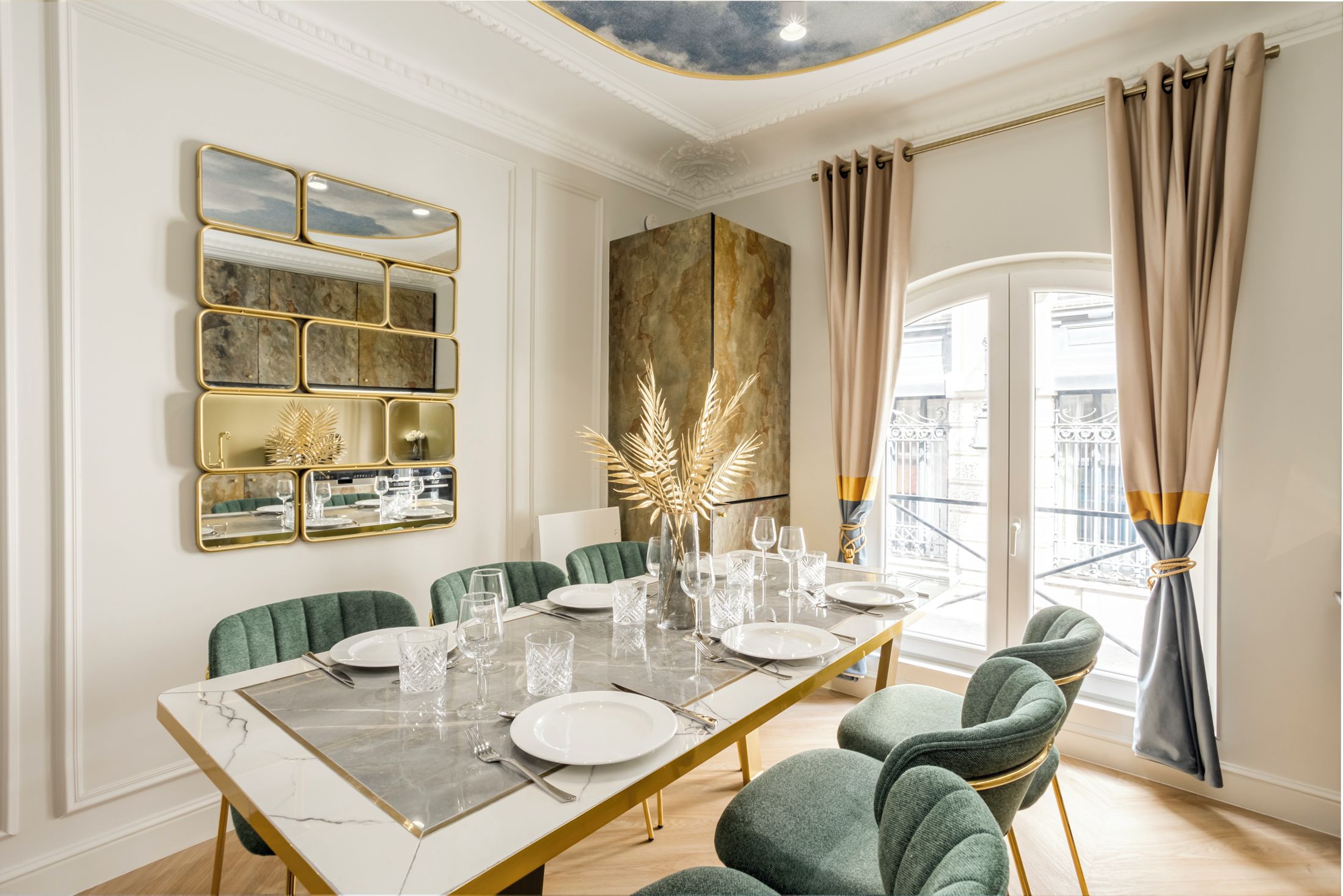 A dining room with a marble table, green upholstered chairs, and a decorative wall piece.