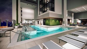 A modern indoor pool with a green wall, lounge chairs, and a cityscape view. - 1BD/Atlanta - Downtown w/Rooftop Pool and Pool Bar! (Atlanta)