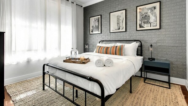Une chambre à coucher moderne, avec un lit, une table de chevet et une grande fenêtre ornée de rideaux légers.