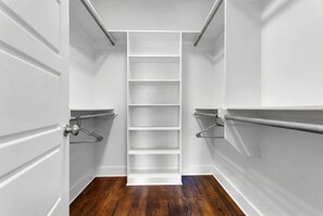 A narrow walk-in closet with white walls, a wooden floor, and multiple shelves.