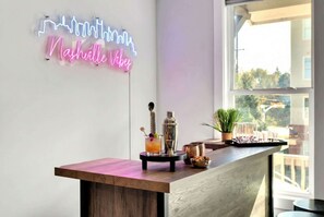 A bar area with a neon sign reading "Nashville Vibes," a cocktail on the bar, and a view of the outdoors through a window.