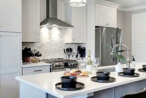 Una cocina moderna con armarios blancos, electrodomésticos de acero inoxidable y una isla central con cuencos negros.