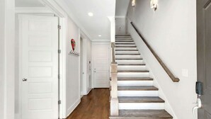 Un couloir avec des portes blanches, un escalier en bois et un luminaire au plafond.