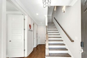 A hallway with white doors, a wooden staircase, and a light fixture above.