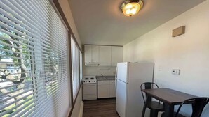 A compact kitchen with white cabinets, a refrigerator, a stove, and a dining table with chairs.