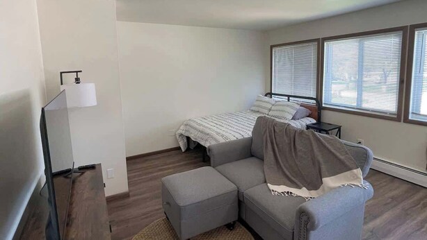 A modern bedroom with a bed, a grey sofa, a small table, and a TV.