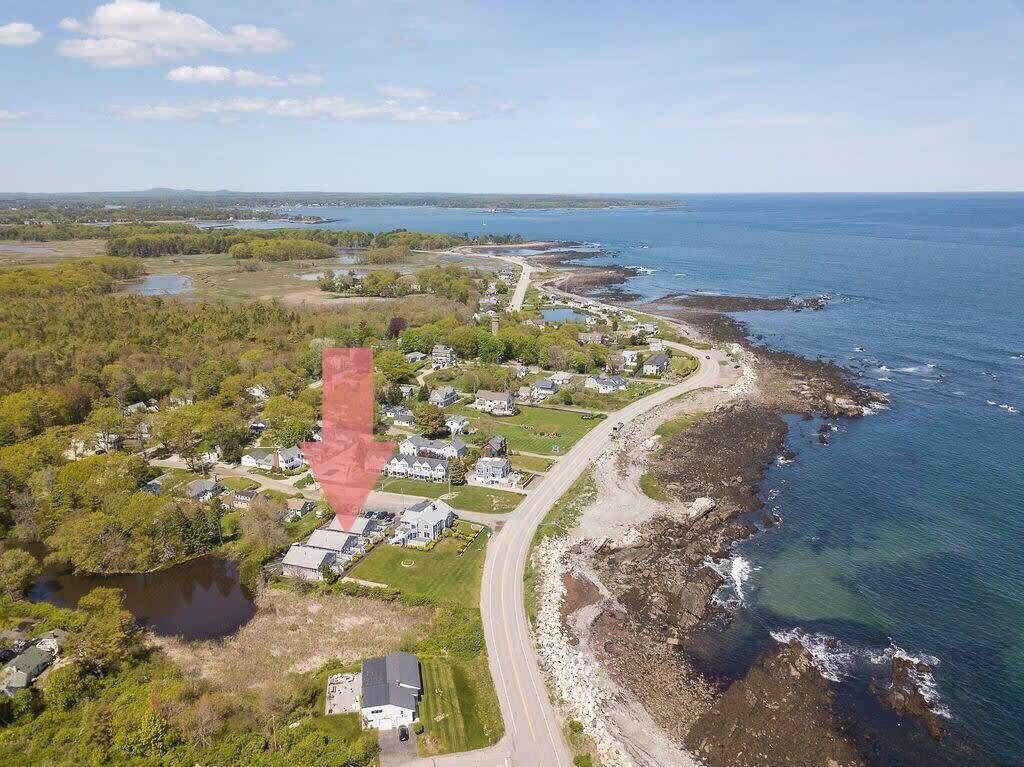 Ilmakuva rannikkoalueen asuinalueesta, jossa talot sijaitsevat rantaviivan varrella, tie kiemurtelee alueen läpi ja talojen vieressä on vesialue.