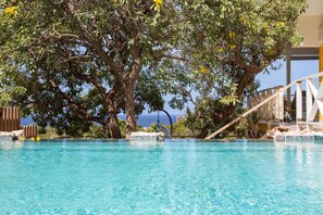 Une piscine d’eau bleue et limpide, avec un arbre en arrière-plan et une vue sur l’océan.