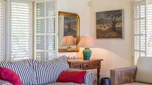 Ein gestreiftes Sofa mit roten Kissen, ein Holztisch mit einer Lampe, ein Schachbrett und ein Bild von einem Baum.
