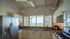 Eine moderne Küche mit weißen Schränken, einem Edelstahlkühlschrank, einem Gasherd und einem großen Fenster mit Jalousien.