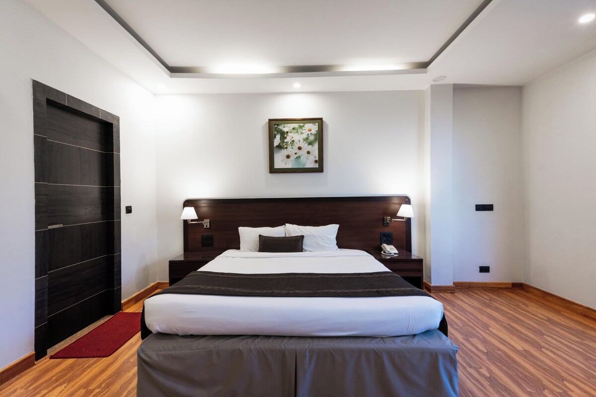 A hotel room with a large bed, bedside lamps, a wooden headboard, a red rug, and a framed picture on the wall.