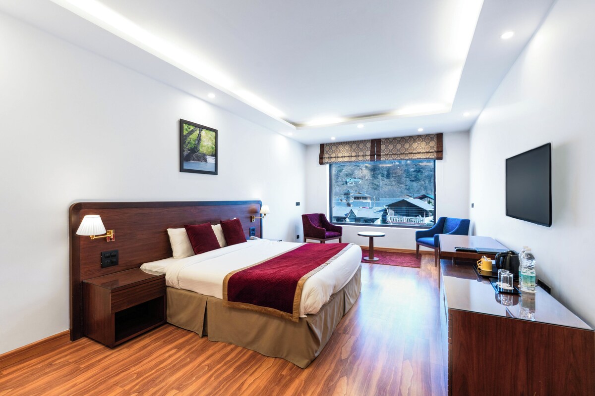 Habitación de hotel moderna con cama, mesita de noche, lámpara y un amplio ventanal con vistas a edificios.