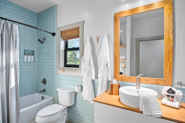A bathroom with a bathtub, toilet, and sink, featuring light blue tiles and a wooden vanity. - Circle A Ranch, Hot tub, Pet Friendly! (Fredericksburg)